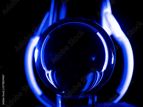 White headphones playing with their reflection in a crystal ball on a black background with blue lighting. Audio concept photo