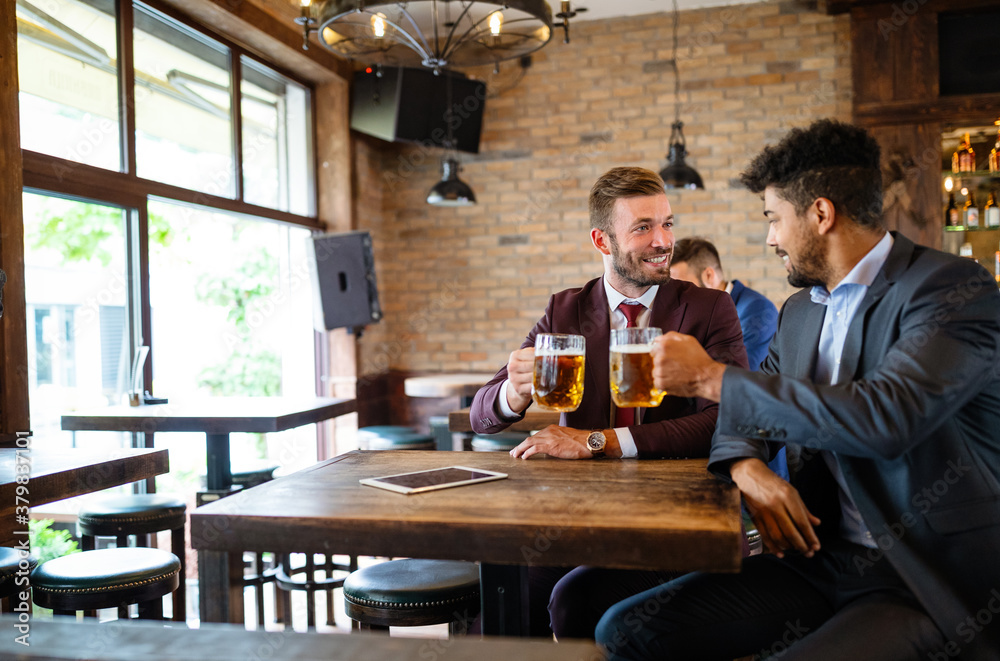 Having a pint with friend. Cheerful young men toasting with beer while sitting together at the bar Having a pint with friend. Cheerful young men toasting with beer while sitting together at the bar