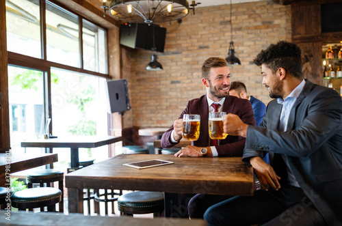 Having a pint with friend. Cheerful young men toasting with beer while sitting together at the bar