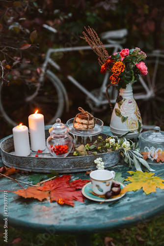 cozy patio. Autumn leaves lie on a wooden antique round table with crockery cups and cookies and candles.