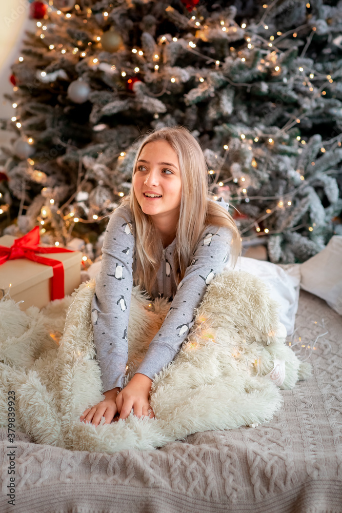 Cheerful cute teen girl opening gifts. Kid wearing pajama having fun near tree in the morning.