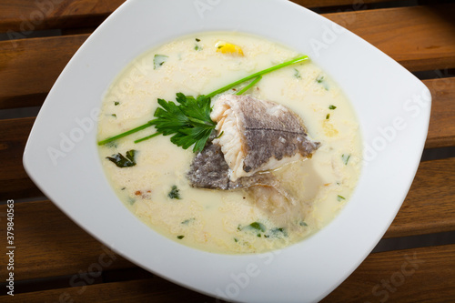 Image of tasty creamy soup with white fish hake and greens at plate