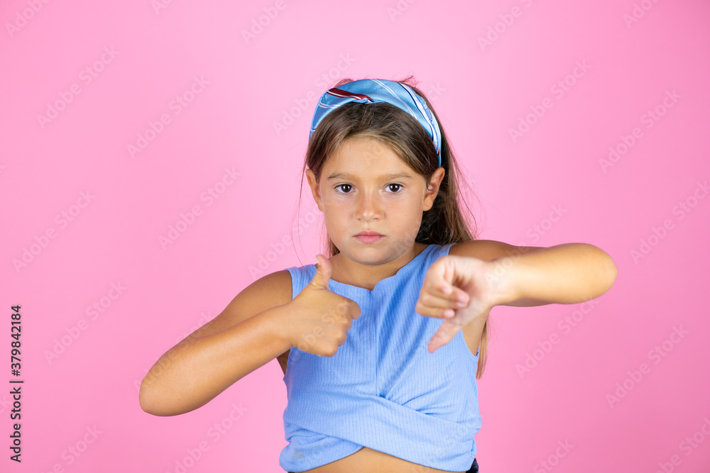 Young beautiful child girl over isolated pink background Doing thumbs up and down, disagreement and agreement expression. Crazy conflict Young beautiful child girl over isolated pink background Doing thumbs up and down, disagreement and agreement expression. Crazy conflict