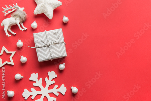 Frame of Christmas white decorations, gift, star, reindeer, snowflake on red background. View from above, flat lay. Xmas greeting card.