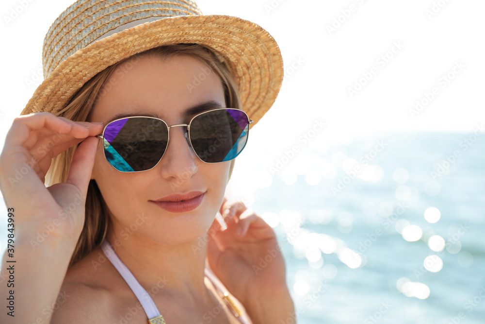 Fototapeta premium Beautiful woman wearing sunglasses near sea on sunny day, closeup