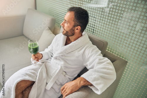 Bearded young man with smoothie sitting on couch in spa salon