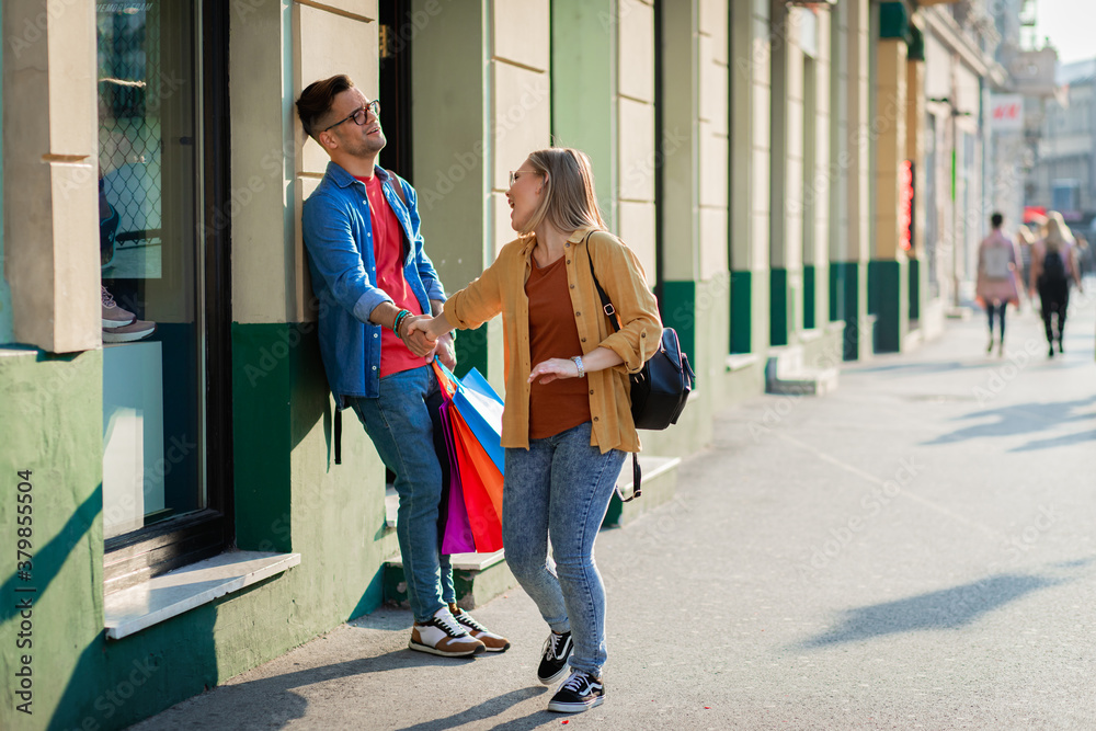 Guy tired of shopping leaning against a wall while a girl full of energy wants to go around more shops.