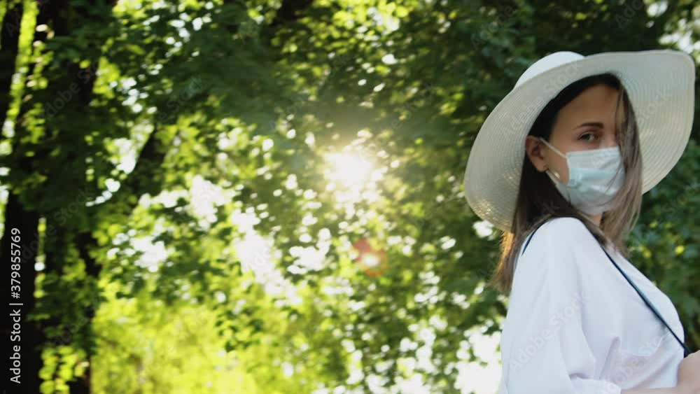 Pandemic restriction. Hygiene protection outdoor. Relaxed woman in white straw hat medicine mask turning on walking in nature green trees park . Quarantine measures. Stay safe. New normal