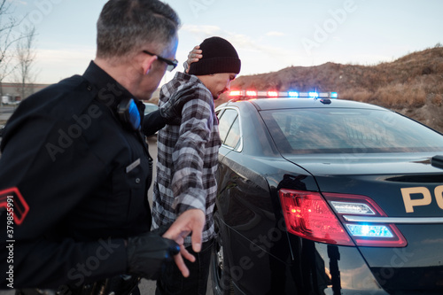A Police Officer searching a suspect beside his cruiser.