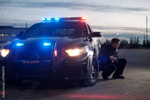 A Police Officer crouches next to a cruiser with his gun drawn photo