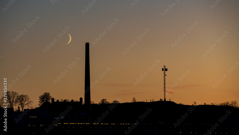Crescent moon near the horizon. Behind the silhouette of the Stockholm skyline.