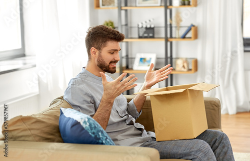 mail delivery, shipment and people concept - disappointed man opening parcel box at home