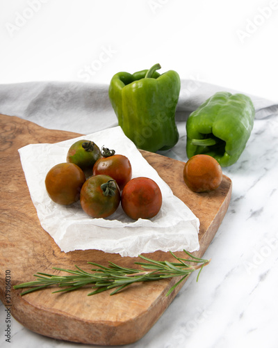 Organic vegetables from kitchen garden on wooden tray.
Green bell peppers and black cherry tomatoes