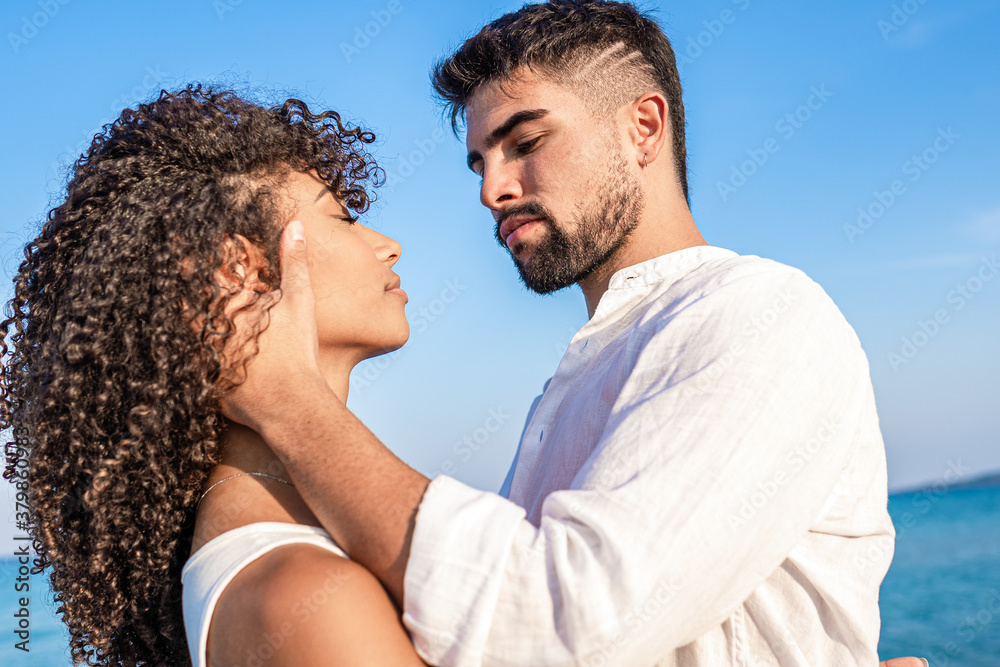 Young handsome bearded man in white shirt grabs his curly hispanic woman forcefully holding her head in his hands with serious expression - Bright and vivid color low angle view Young handsome bearded man in white shirt grabs his curly hispanic woman forcefully holding her head in his hands with serious expression - Bright and vivid color low angle view
