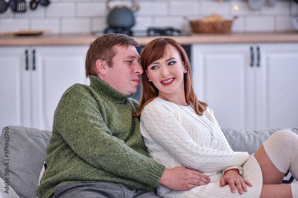 A loving couple in warm knitted sweaters hug and kiss. Lovers celebrate New Year at home, sit in the white kitchen by the Christmas tree, hold hands, look at each other. Close up portraite, copy space