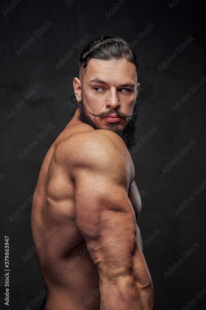 Handsome and muscular guy with beard and modern hairstyle posing in dark gray background.