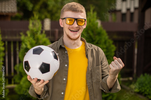 Excited young man with soccer ball smiling, Happy male football fan support sport team, celebrating victory outdoors. People emotions, sports, entertainment concept, successful bet on sports