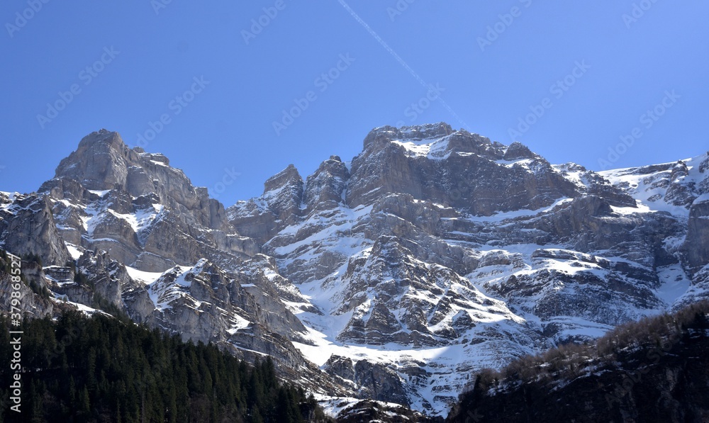 Peaks of Alps mountains surrounding Klöntalersee lake in Klöntal, Kloental valley, during sunny spring day  in Schwyz Alps, canton Glarus, Switzerland. Mountains are covered with snow.