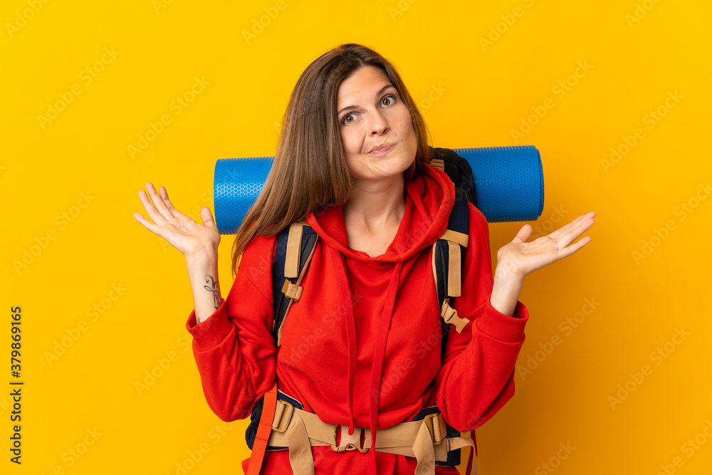 Slovak mountaineer woman with a big backpack isolated on yellow background having doubts while raising hands Slovak mountaineer woman with a big backpack isolated on yellow background having doubts while raising hands