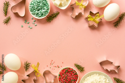 Fototapeta Naklejka Na Ścianę i Meble -  Flat lay of christmas cookie cutters and baking ingredients on a pink background. Space for text
