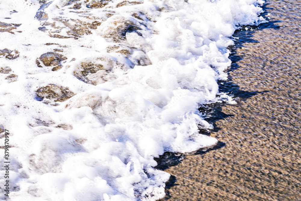 Close up of bubbling sea wave rolling over sand beach