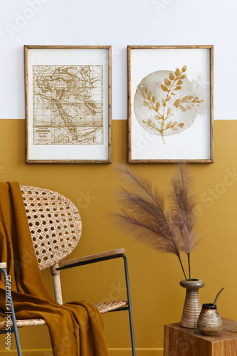 Stylish composition of living room interior with design rattan armchair, two mock up poster frames, plants, cube, palid and personal accessories in honey yellow home decor. Template. photo