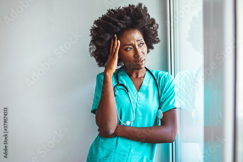 Tired female nurse in hospital corridor. Young female healthcare worker having an headache and touching her head in hospital lobby. Nurse doctor with migraine overworked, over stressed photo