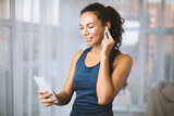 Hispanic woman with earphones and cell phone listening to music during her training in gym