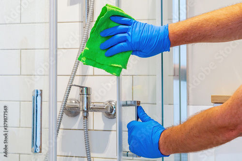 The cleaner washes shower door in bathroom with detergents. Bathroom cleaning idea