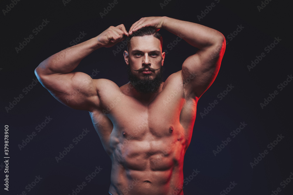 Muscular guy with black beard and mustache staying and combing his hairs in dark studio background. Muscular guy with black beard and mustache staying and combing his hairs in dark studio background.