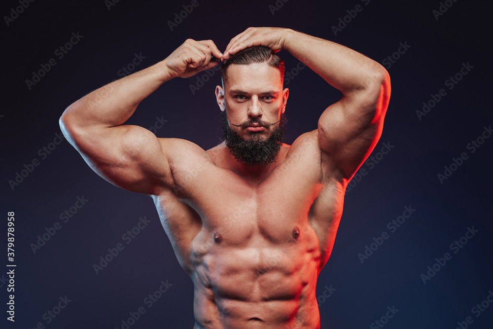 Brutal and muscular bodybuilder with dark beard posing with and combing