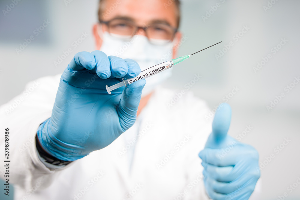doctor with gloves and face mask presenting a syringe with Covid-19 vaccine