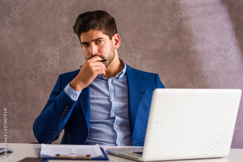 Businessman looking thoughtfully while sitting at desk and working on laptop
