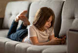 
the child lies on the couch and looks at the phone