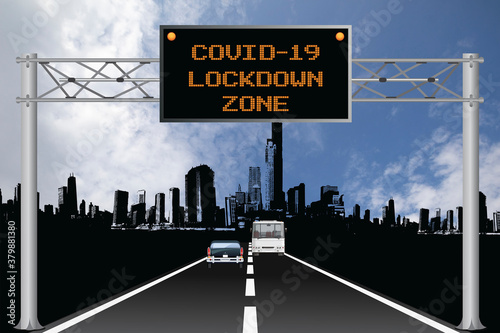 Roadway overhead digital gantry sign with COVID 19 Coronavirus lockdown zone message set against a blue cloudy sky 