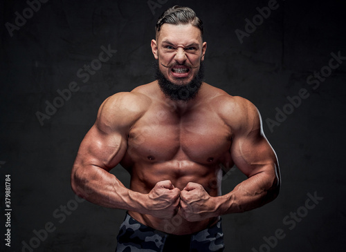 Self confident and aggressive military bodybuilder with naked torso and with black beard posing in gray background. © Fxquadro