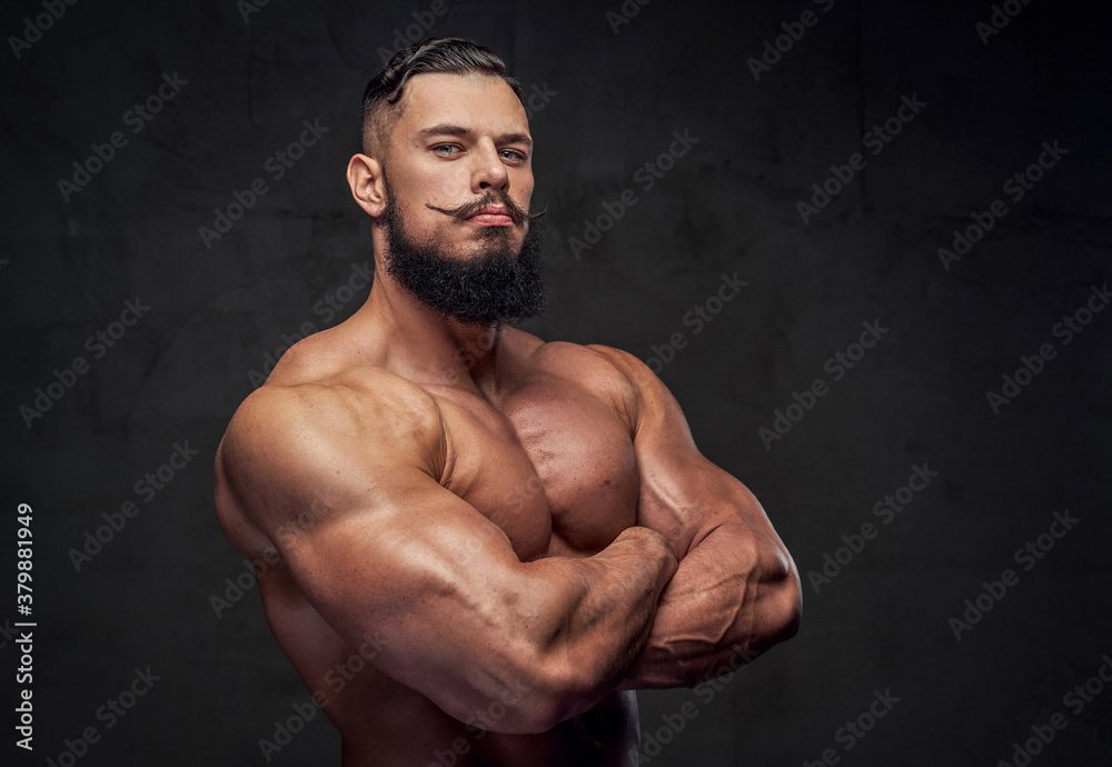 Handsome bearded bodybuilder with naked torso and with modern hairstyle posing with crossed arms.