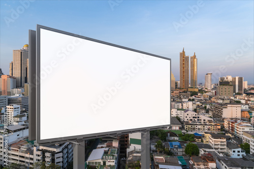 Blank white road billboard with Bangkok cityscape background at sunset. Street advertising poster, mock up, 3D rendering. Side view. The concept of marketing communication to promote or sell idea.