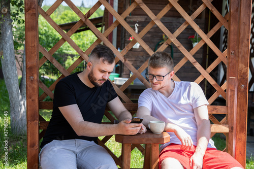 Young men talking outdoors in coutryside, two male friends looking at mobile phone screen, testing internet application. Employment for creative professions, programmers, home office, lifestyle