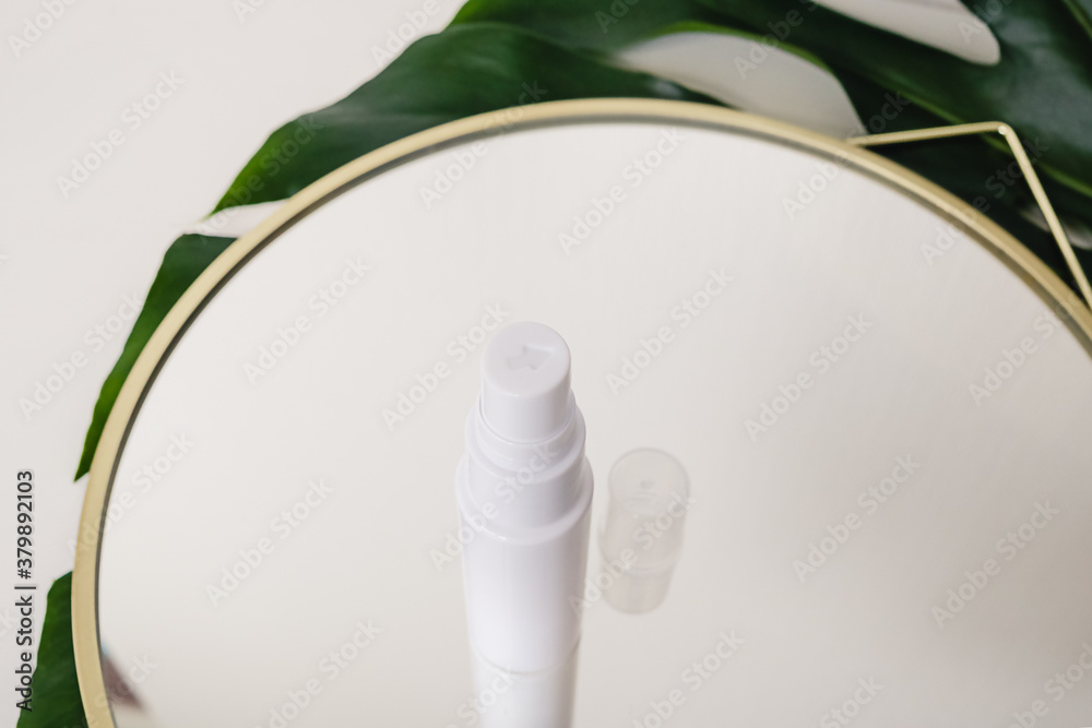 Plastic spray dispenser for cosmetics, natural medicine , essential oils or other liquid on a white background standing on a mirror decorated with a green monstera leaf - obrazy, fototapety, plakaty 