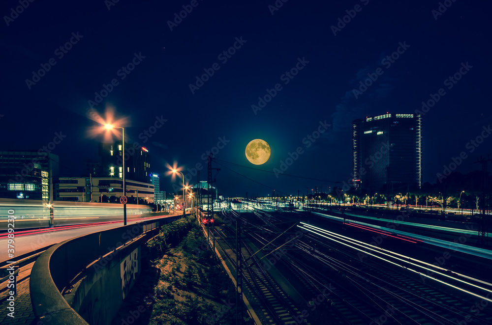 Mannheim, Germany. July 2th, 2015. Creative night image of Mannheim Central Station with light trails of running trains and a big full Moon. On the right the Victoria Tower skyscraper.