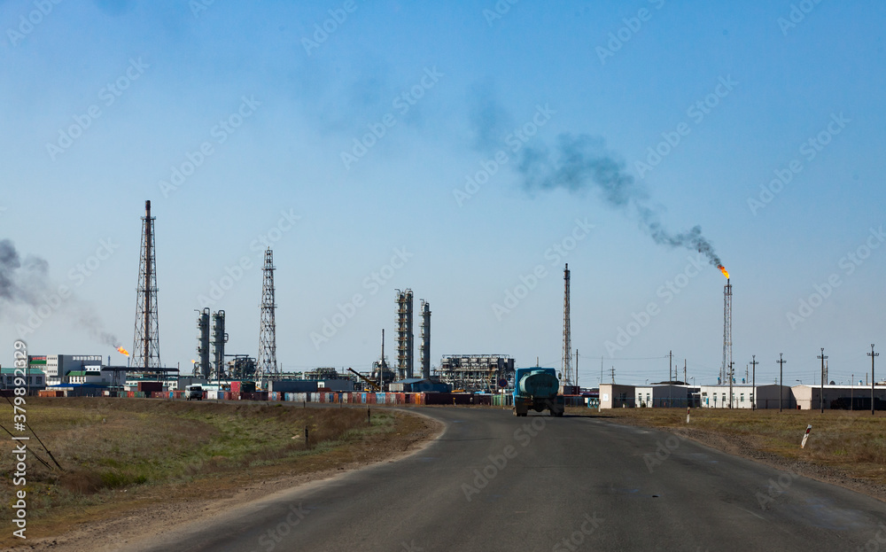 Oil refinery and gas processing plant. View of communication tower, refining columns, gas torch mast, pipelines and industrial building against clear blue sky. Oil refinery and gas processing plant. View of communication tower, refining columns, gas torch mast, pipelines and industrial building against clear blue sky.