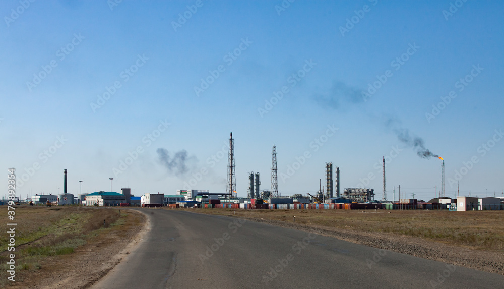 Oil refinery and gas processing plant. View of communication tower, refining columns, gas torch mast, pipelines and industrial building against clear blue sky. Oil refinery and gas processing plant. View of communication tower, refining columns, gas torch mast, pipelines and industrial building against clear blue sky.