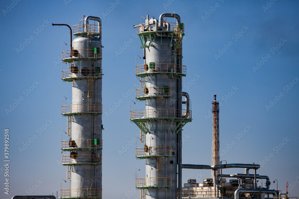 Close-up of oil Grey distillation towers (refining columns) on blue sky. On petrochemical plant. Gas torch tower on background.