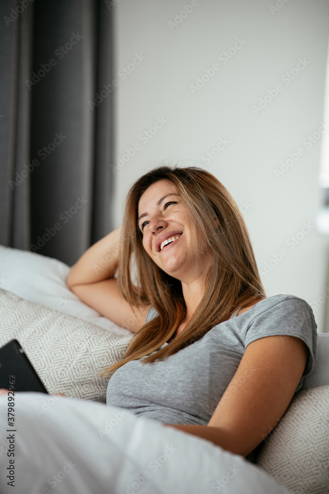 Young beautiful woman using phone in bed. Girl lying on bed.. Young beautiful woman using phone in bed. Girl lying on bed..