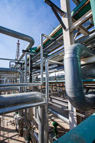 Oil refinery plant. Tubes and pipelines and gas torch tower on blue sky Abstract industrial background.