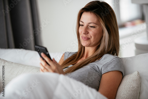 Young beautiful woman using phone in bed. Girl lying on bed..