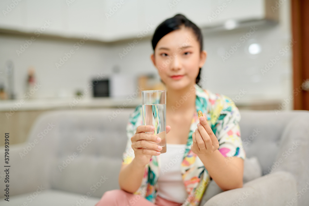 Happy woman taking a vitamin yellow pill sitting on a couch in the living room at home Happy woman taking a vitamin yellow pill sitting on a couch in the living room at home