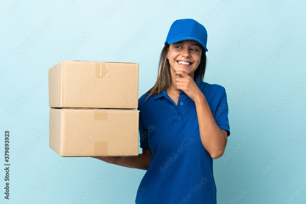 Young delivery woman isolated on blue background looking to the side and smiling Young delivery woman isolated on blue background looking to the side and smiling