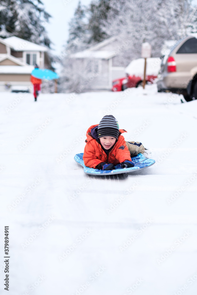 Asian boy sledding on the street outside their home Asian boy sledding on the street outside their home